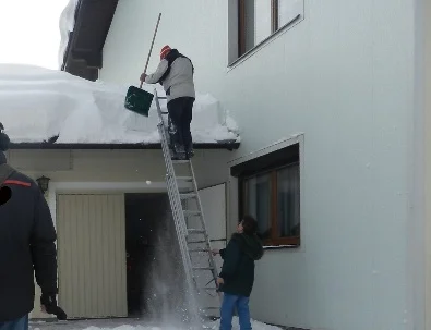 Zwei Personen räumen Schnee von einem Vordach
