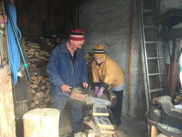 Ein Mann und eine Frau sägen gemeinsam Brennholz in einem Schuppen.