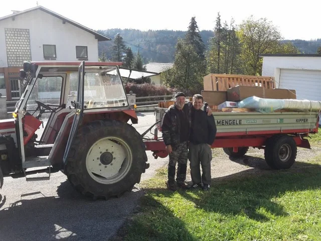 Zwei Männer stehen vor einem Traktor mit einem Anhänger voller Umzugsgut.